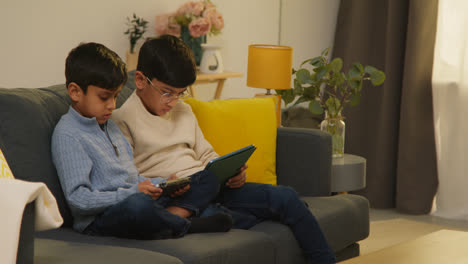 Two-Young-Boys-Sitting-On-Sofa-At-Home-Playing-Games-Or-Streaming-Onto-Digital-Tablets-10